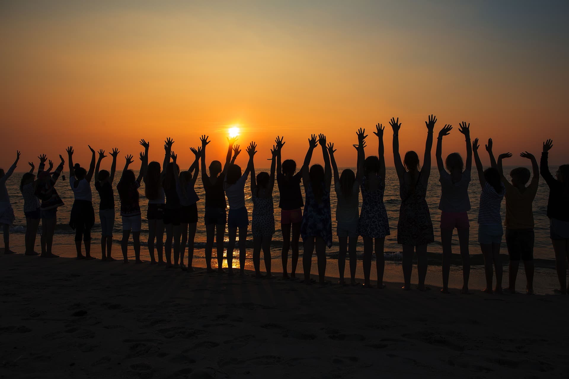 На закате группа людей подняли руки вверх на побережье